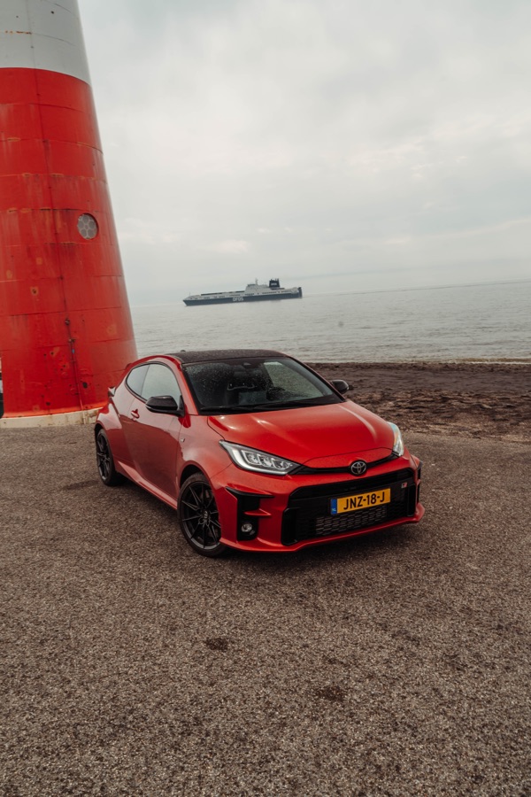 Rode Toyota GR Yaris bij een vuurtoren aan zee
