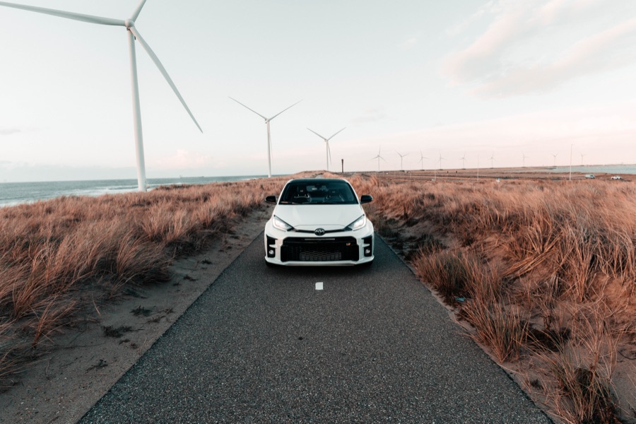 Witte Toyota GR Yaris op een duinweg met windmolens